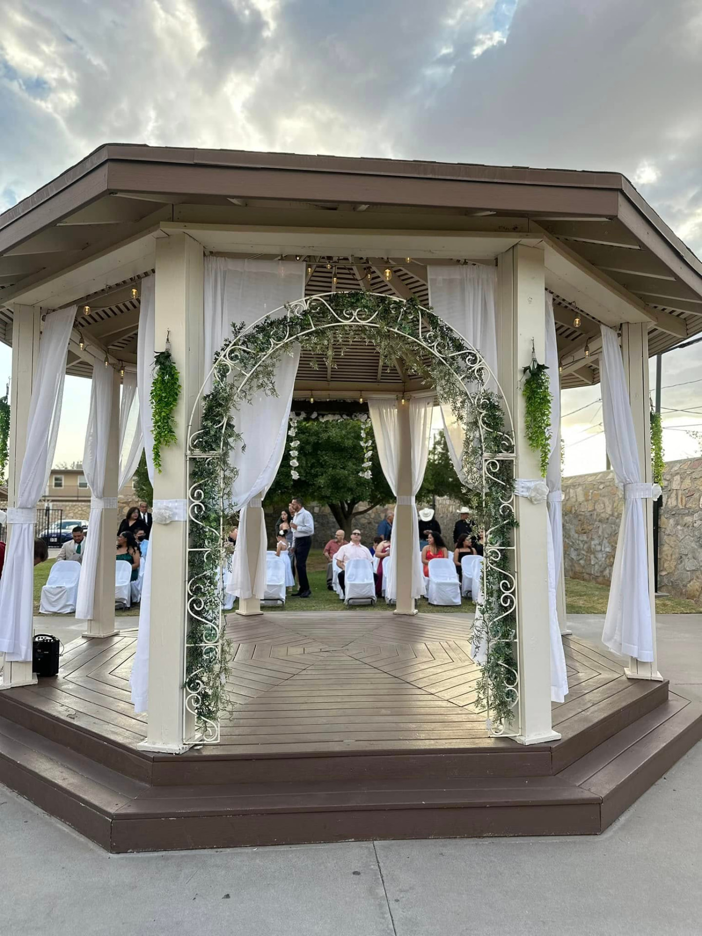 An outdoor gazebo ceremony site at EPMPOA Memorial Hall with a white floral arch and guest chairs