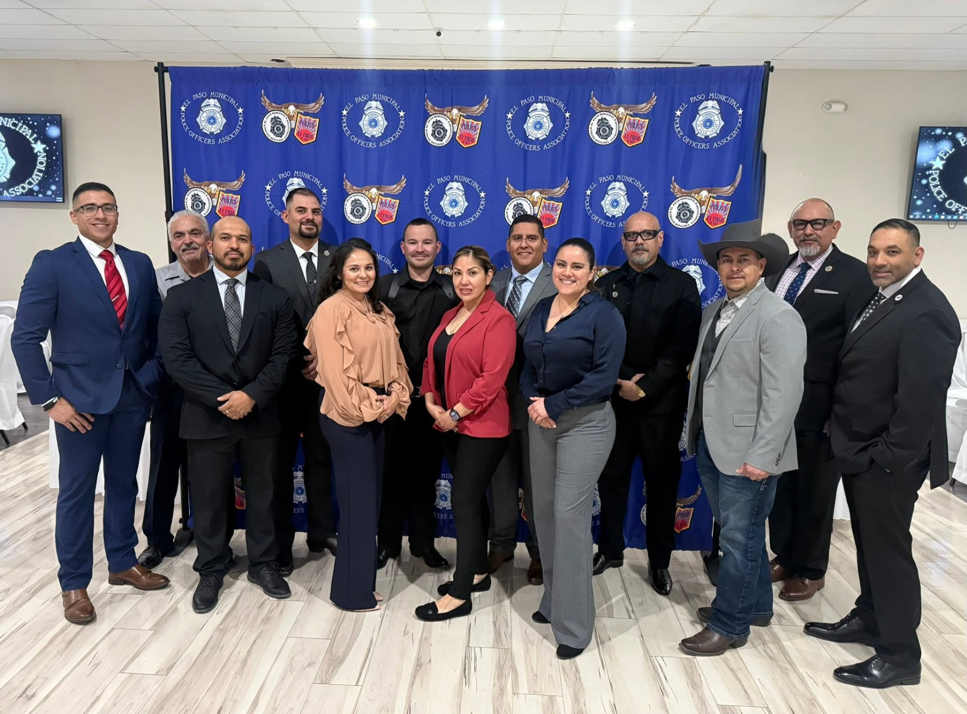 A group portrait of thirteen EPMPOA members posing together in front of the El Paso Municipal Police Officers Association backdrop
