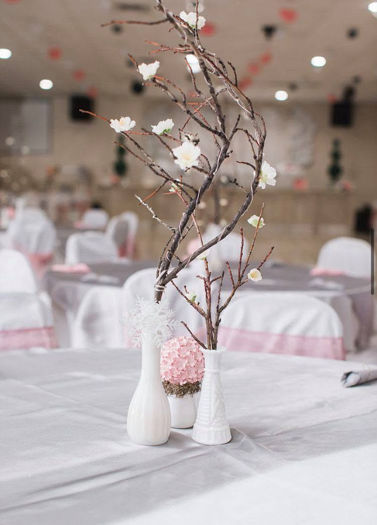 A banquet table centerpiece of white ceramic vases with branches and a pink floral ball at EPMPOA Memorial Hall